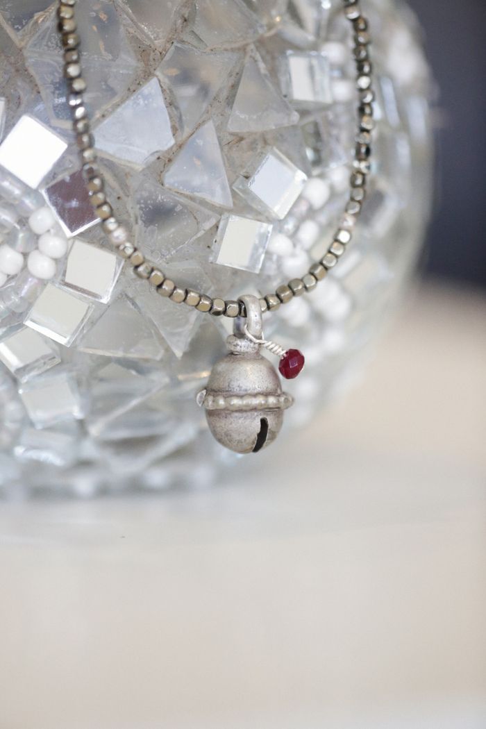 Close-up of a silver necklace with a small bell charm against a textured backdrop.