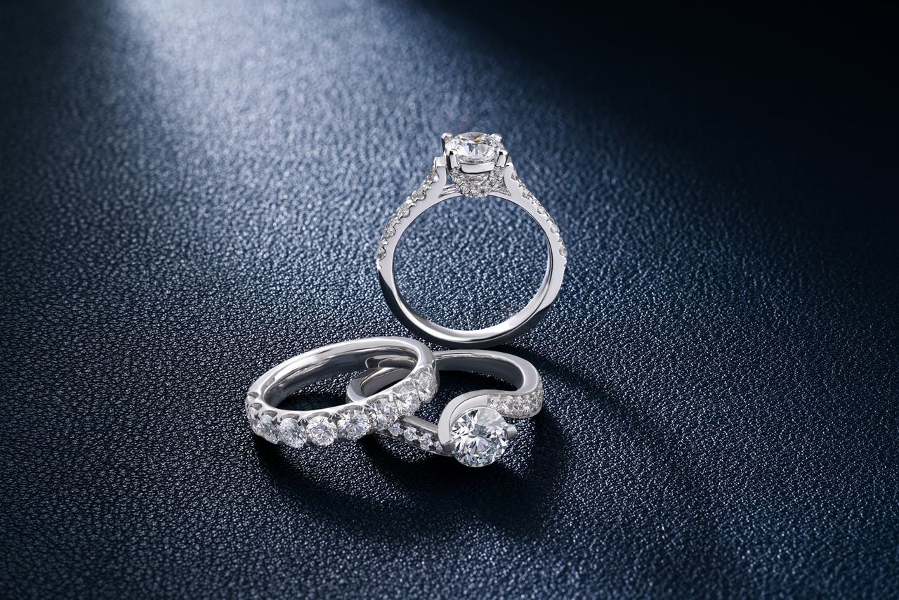 Home Close-up of luxurious diamond engagement and wedding rings on a textured surface, showcasing elegance and craftsmanship.