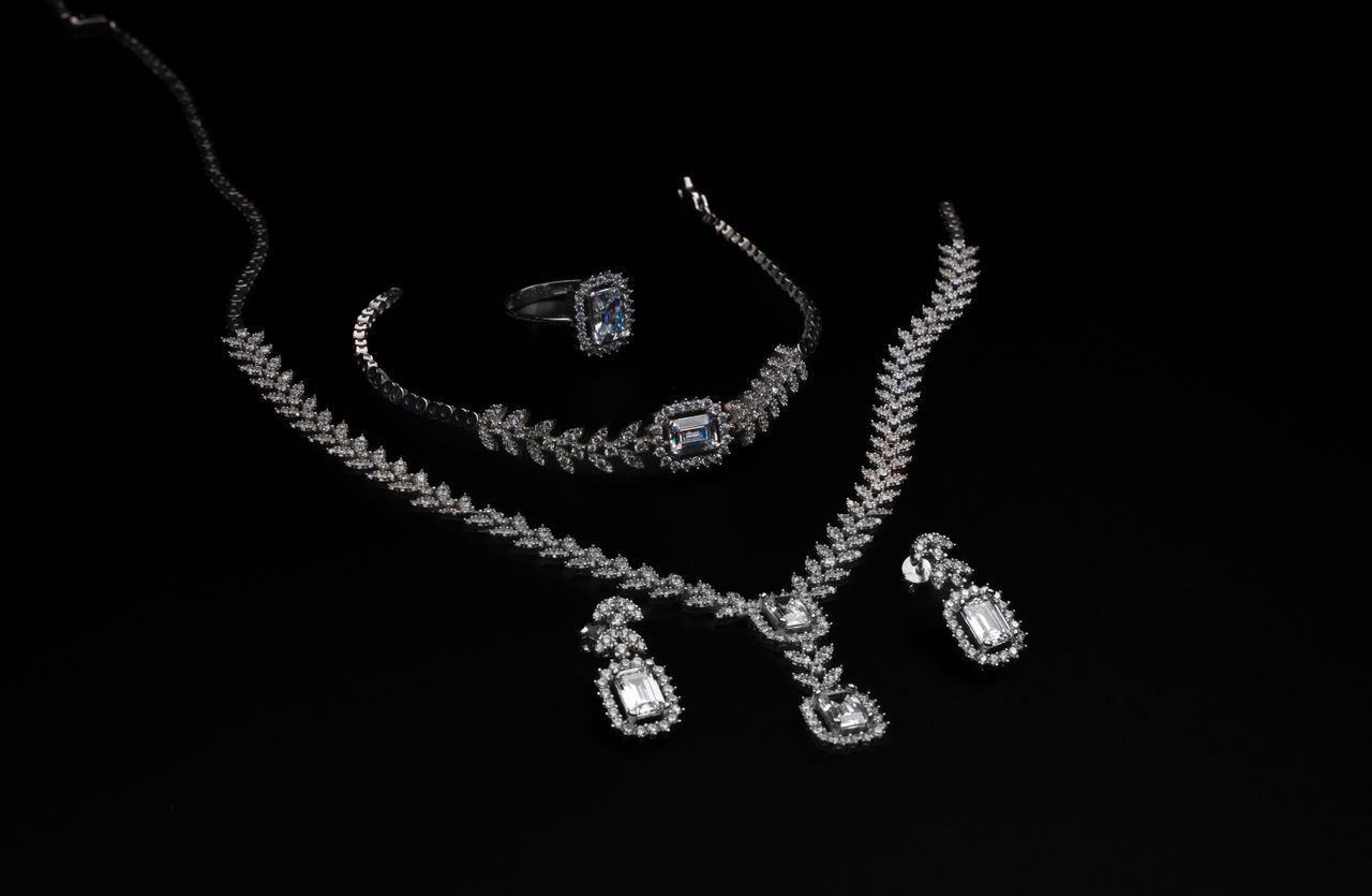 Elegant diamond jewelry set including necklace, bracelet, ring, and earrings on a black backdrop.