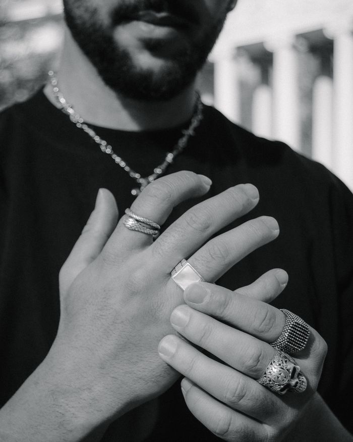 Monochrome close-up of a person's hands adorned with multiple silver rings, emphasizing style and elegance.